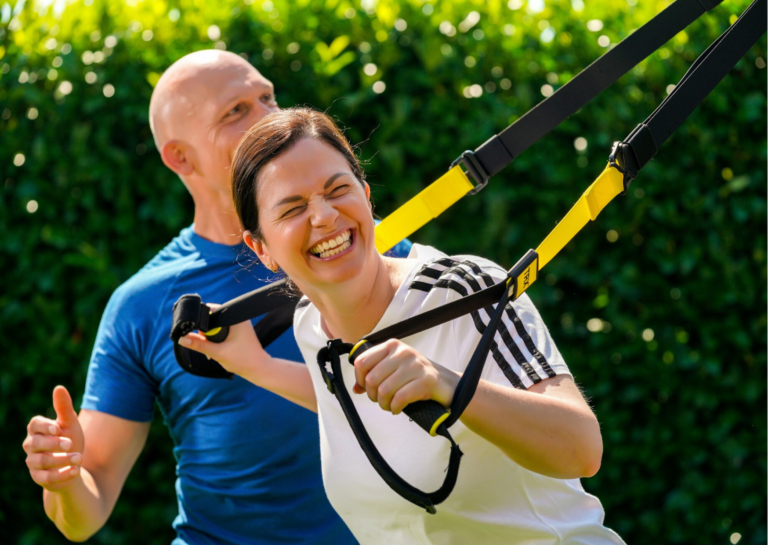Personal Trainer Bernd Wolfgang trainiert mit einer Klientin am TRX-Band im Garten
