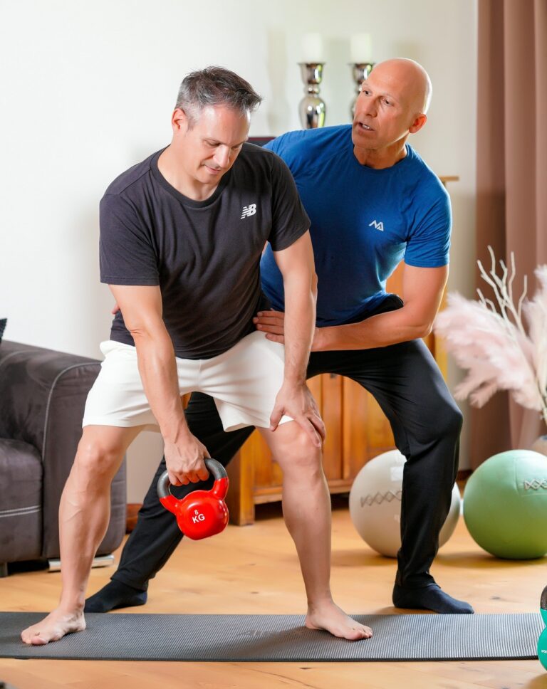 Personal Trainer Bernd Wolfgang trainiert einen Klienten mit Kettlebell in einem Wohnzimmer