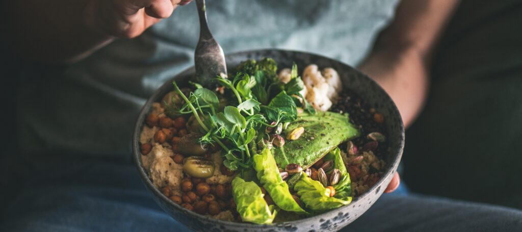 Person hält eine nährstoffreiche Bowl mit frischem Gemüse, Avocado, Hülsenfrüchten und Samen