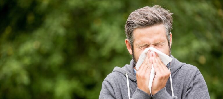 Mann in sportlicher Kleidung niest in ein Taschentuch im Freien